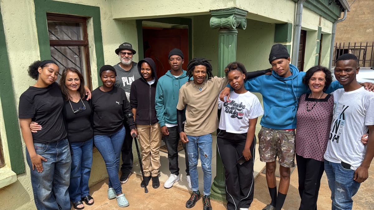 Eleven volunteers and young people standing close together with their arms around each other outside a pale green house